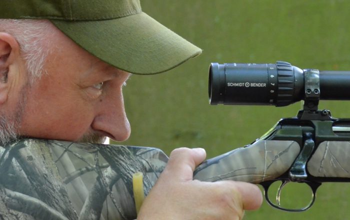 Ein Jäger hält sein Gewehr und visiert sein Wild durch das Zielrohr an.