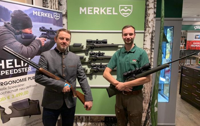 Ein Jagsschule Lüdersburg Mitarbeiter steht mit einem Jäger an einem Merkel Gewehre Stand in einem Fachgeschäft.